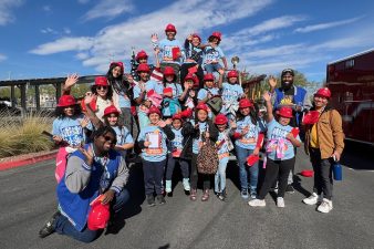 A group of students wear red firefighter hats while waving.